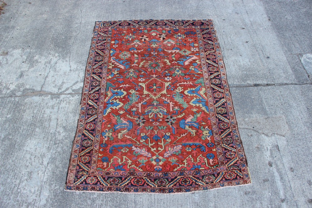 An antique hand-knotted Heriz carpet featuring a terracotta red field with central geometric motifs and a navy blue patterned border. View XV