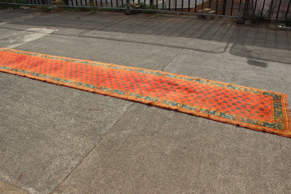 An extra long, narrow antique Turkish Oushak runner featuring a terracotta central field with small repeating geometric motifs enclosed within a dark blue-green patterned border. View II
