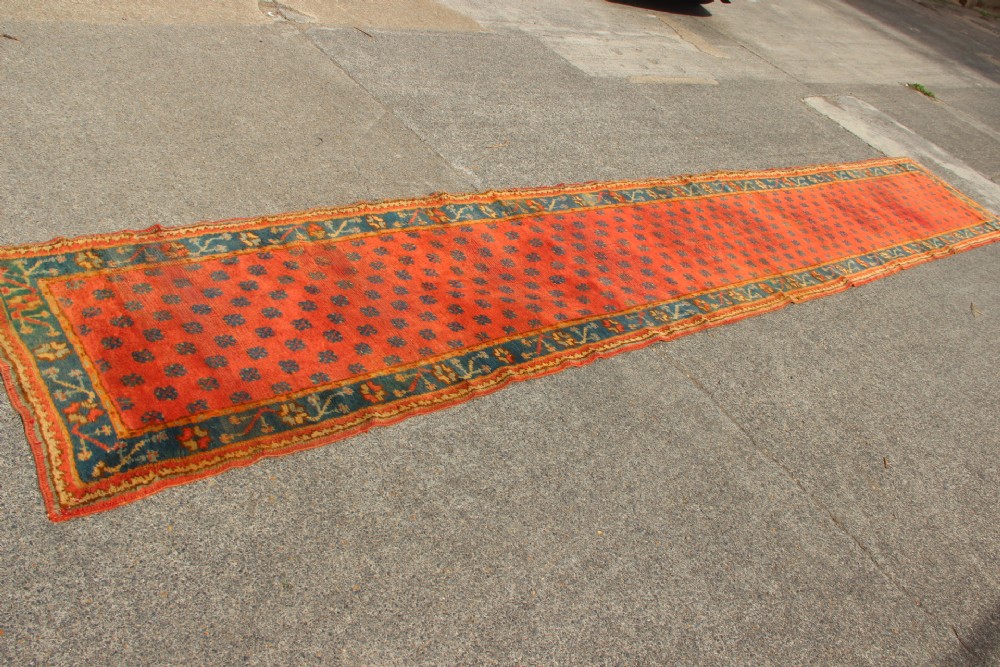 An extra long, narrow antique Turkish Oushak runner featuring a terracotta central field with small repeating geometric motifs enclosed within a dark blue-green patterned border. View III