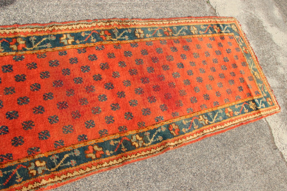 An extra long, narrow antique Turkish Oushak runner featuring a terracotta central field with small repeating geometric motifs enclosed within a dark blue-green patterned border. View VI