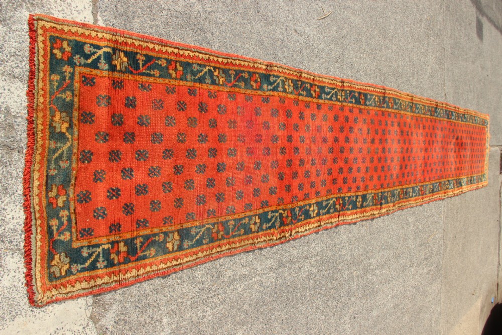An extra long, narrow antique Turkish Oushak runner featuring a terracotta central field with small repeating geometric motifs enclosed within a dark blue-green patterned border. View VII