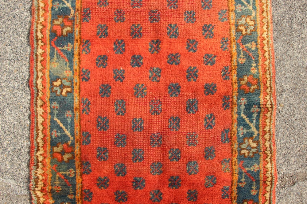 An extra long, narrow antique Turkish Oushak runner featuring a terracotta central field with small repeating geometric motifs enclosed within a dark blue-green patterned border. View V