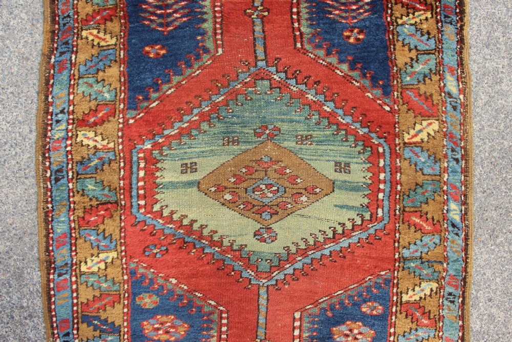 An antique North West Persian long hallway runner rug with a red and blue field, featuring geometric diamond medallions and a stylized leaf border. View II