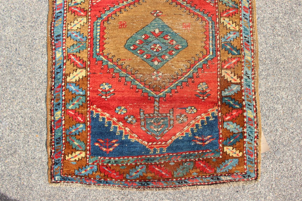An antique North West Persian long hallway runner rug with a red and blue field, featuring geometric diamond medallions and a stylized leaf border. View III