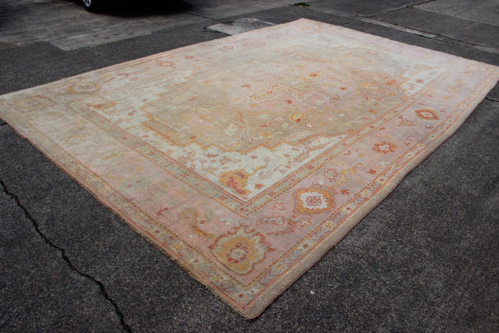 A large hand-knotted wool Oushak carpet displaying a central star medallion, angular floral spandrels, and a pastel palette of pale pink, cream, and beige. View II