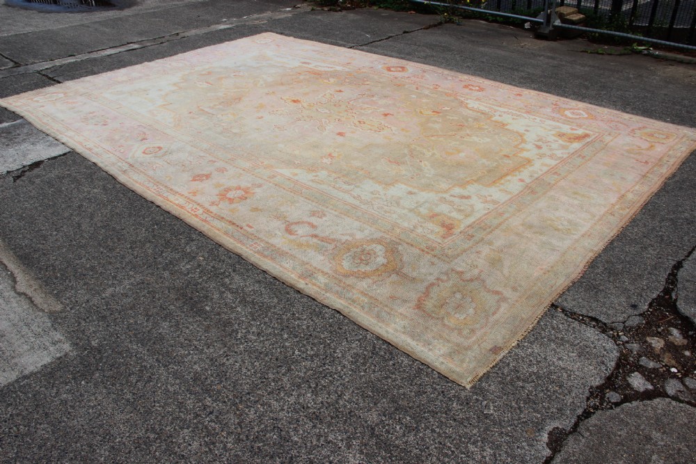 A large hand-knotted wool Oushak carpet displaying a central star medallion, angular floral spandrels, and a pastel palette of pale pink, cream, and beige. View III