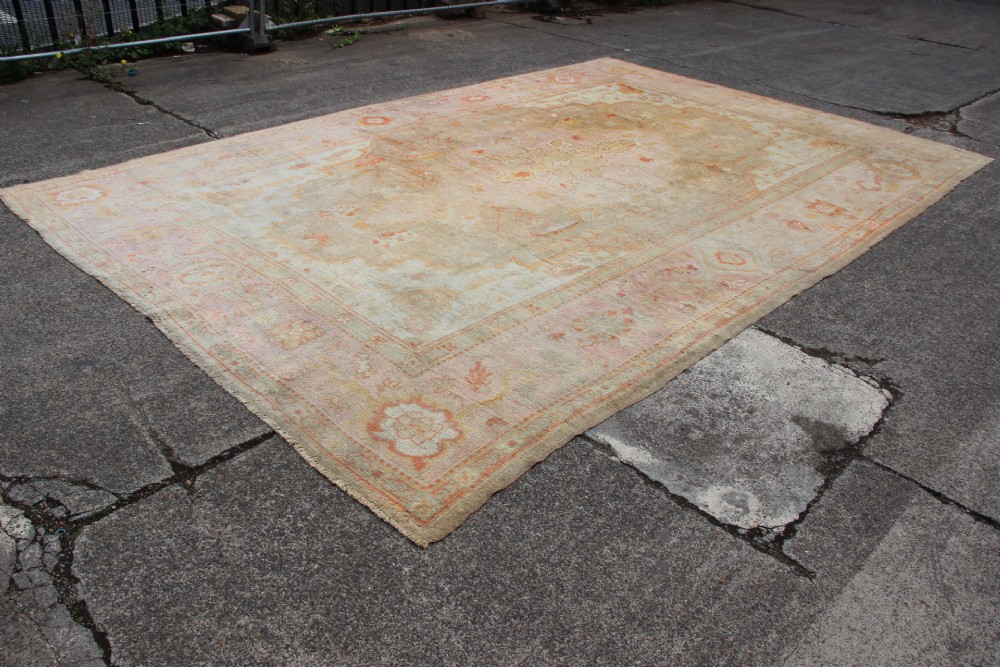A large hand-knotted wool Oushak carpet displaying a central star medallion, angular floral spandrels, and a pastel palette of pale pink, cream, and beige. View IV