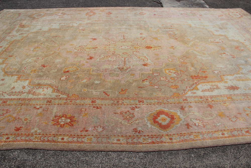 A large hand-knotted wool Oushak carpet displaying a central star medallion, angular floral spandrels, and a pastel palette of pale pink, cream, and beige. View V
