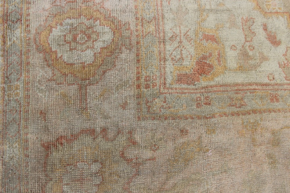 A large hand-knotted wool Oushak carpet displaying a central star medallion, angular floral spandrels, and a pastel palette of pale pink, cream, and beige. View VII