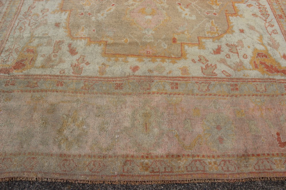A large hand-knotted wool Oushak carpet displaying a central star medallion, angular floral spandrels, and a pastel palette of pale pink, cream, and beige. View VIII