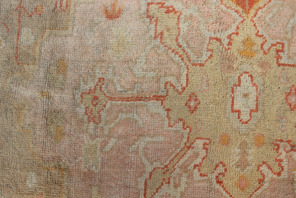 A large hand-knotted wool Oushak carpet displaying a central star medallion, angular floral spandrels, and a pastel palette of pale pink, cream, and beige. View IX