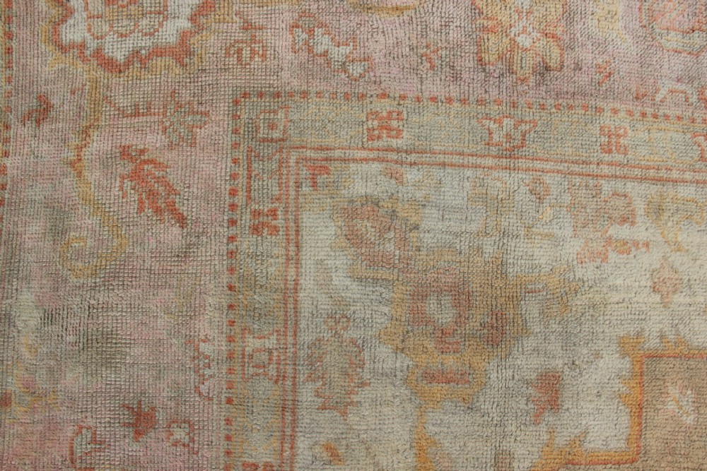 A large hand-knotted wool Oushak carpet displaying a central star medallion, angular floral spandrels, and a pastel palette of pale pink, cream, and beige. View X