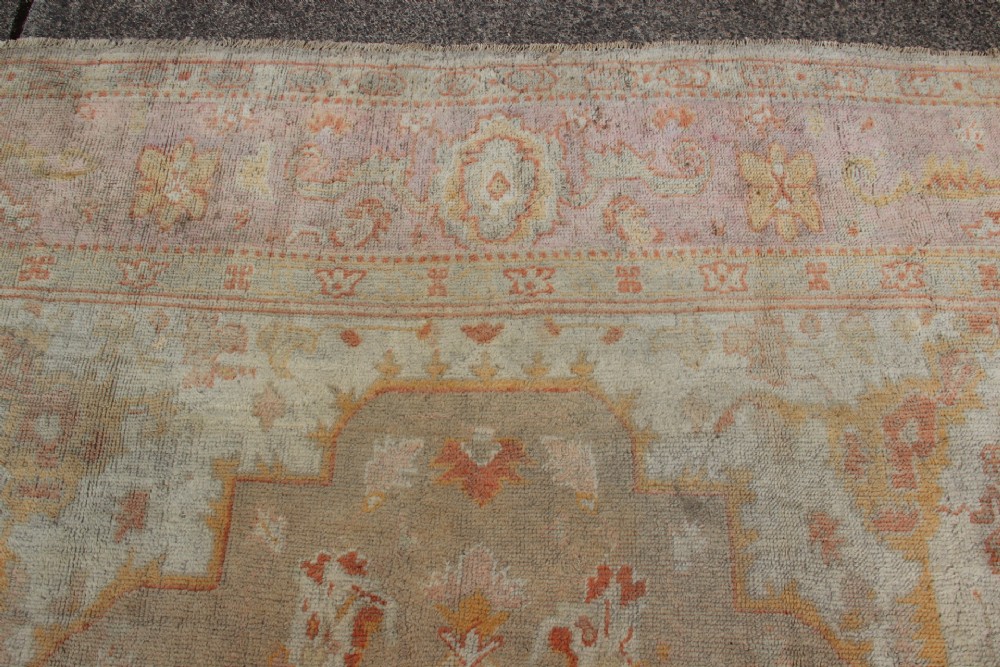 A large hand-knotted wool Oushak carpet displaying a central star medallion, angular floral spandrels, and a pastel palette of pale pink, cream, and beige. View XI