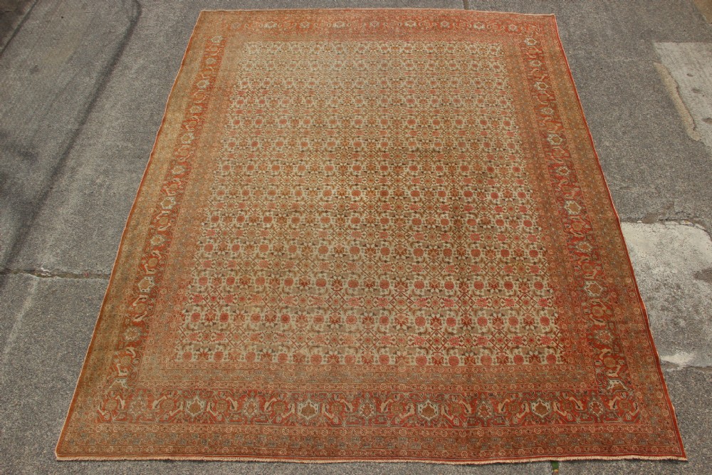 A large rectangular hand-knotted Persian Tabriz wool carpet featuring an all-over repeating geometric and floral pattern in terracotta, rust red, and beige framed by a complex multi-band border.