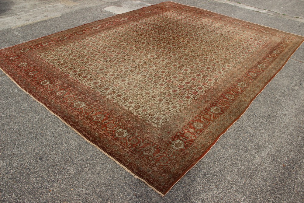 A large rectangular hand-knotted Persian Tabriz wool carpet featuring an all-over repeating geometric and floral pattern in terracotta, rust red, and beige framed by a complex multi-band border. View X