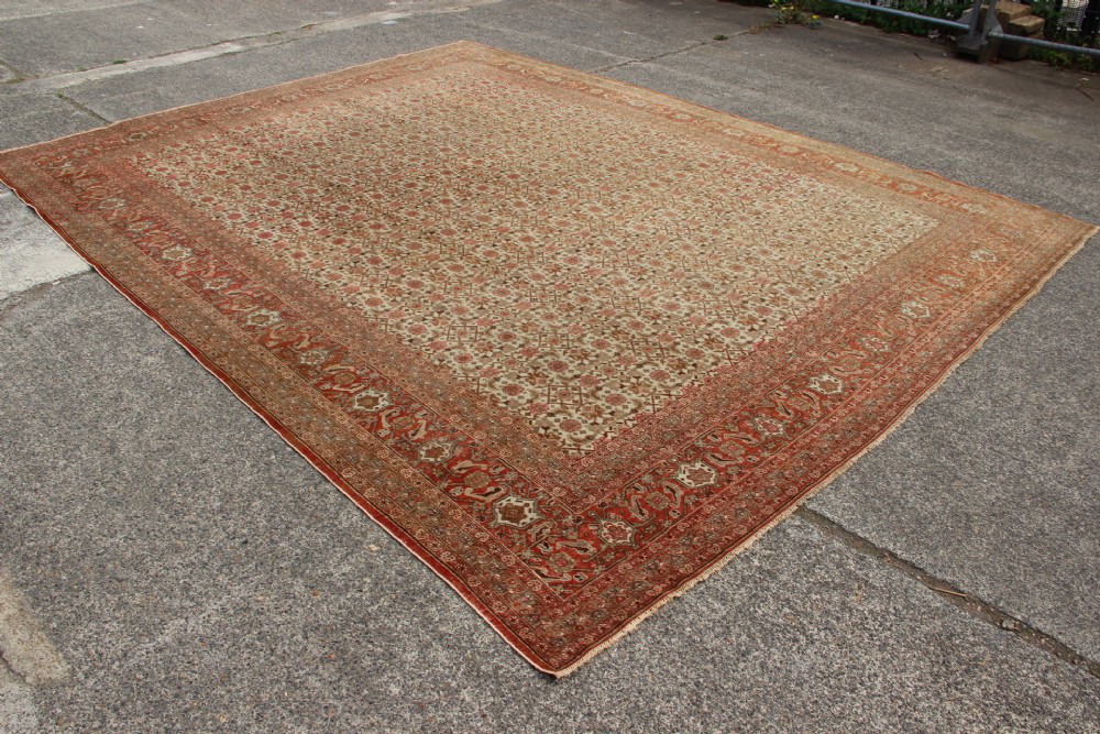 A large rectangular hand-knotted Persian Tabriz wool carpet featuring an all-over repeating geometric and floral pattern in terracotta, rust red, and beige framed by a complex multi-band border. View XII