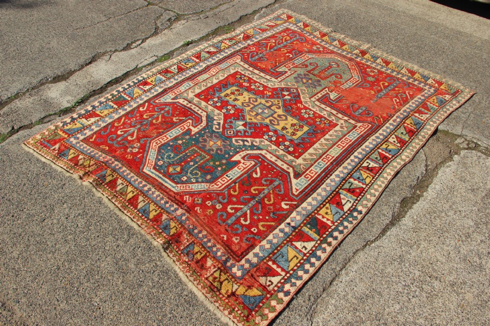 A hand-knotted Caucasian rug featuring a central red and blue shield medallion framed by geometric borders on a red field. View II