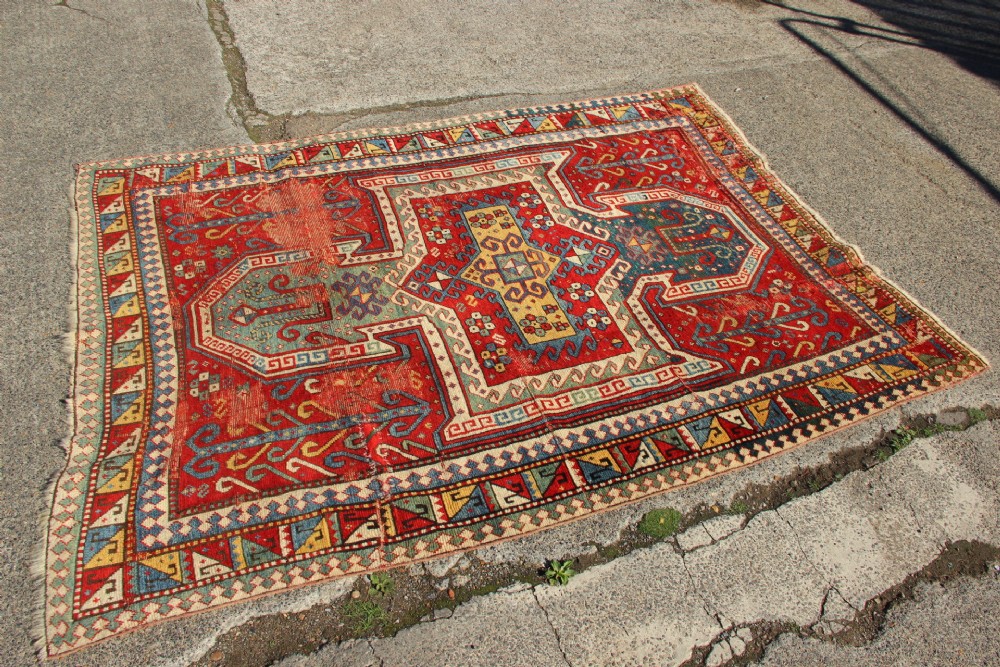 A hand-knotted Caucasian rug featuring a central red and blue shield medallion framed by geometric borders on a red field. View XII