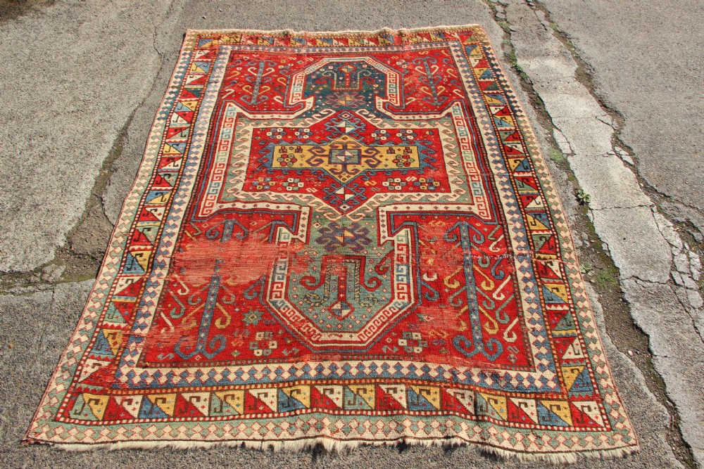 A hand-knotted Caucasian rug featuring a central red and blue shield medallion framed by geometric borders on a red field. View XIII