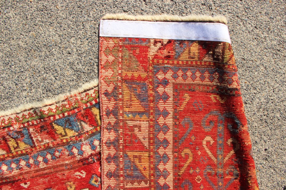 A hand-knotted Caucasian rug featuring a central red and blue shield medallion framed by geometric borders on a red field. View XIV