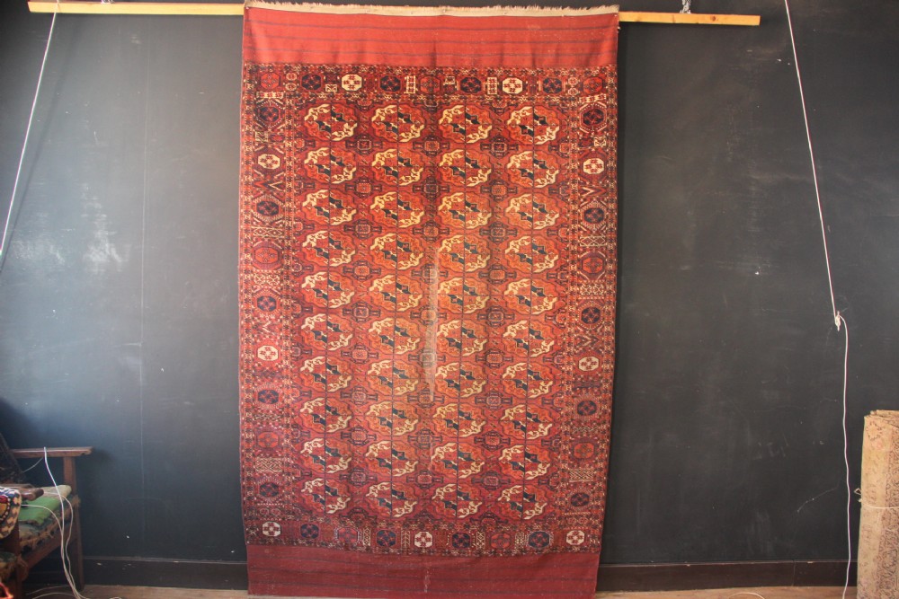 A large mid-19th century Tekke Turkoman hand-knotted wool main carpet featuring repeating geometric gol motifs on a deep red field with woven borders.