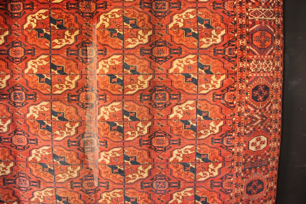 A large mid-19th century Tekke Turkoman hand-knotted wool main carpet featuring repeating geometric gol motifs on a deep red field with woven borders. View II