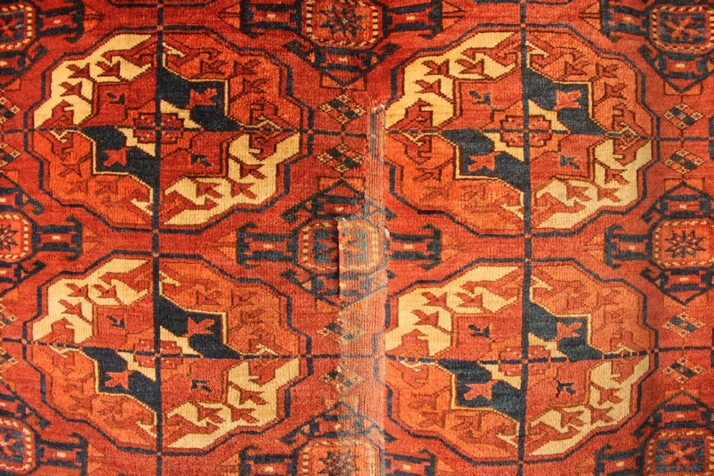 A large mid-19th century Tekke Turkoman hand-knotted wool main carpet featuring repeating geometric gol motifs on a deep red field with woven borders. View III