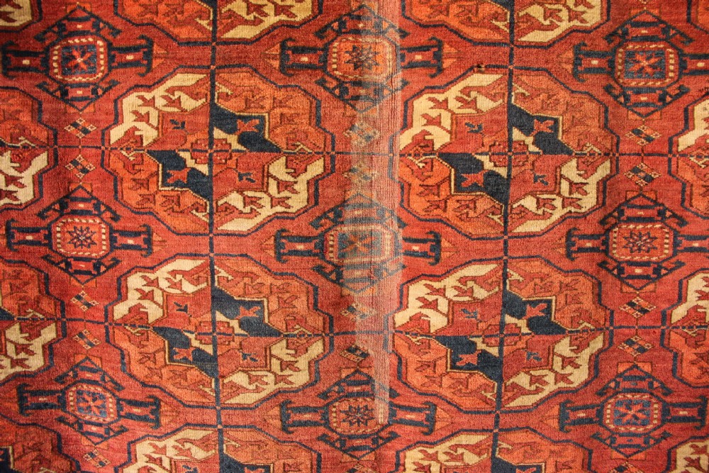 A large mid-19th century Tekke Turkoman hand-knotted wool main carpet featuring repeating geometric gol motifs on a deep red field with woven borders. View IV