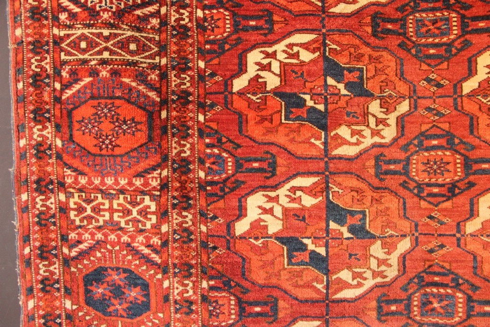 A large mid-19th century Tekke Turkoman hand-knotted wool main carpet featuring repeating geometric gol motifs on a deep red field with woven borders. View V