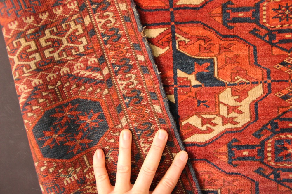 A large mid-19th century Tekke Turkoman hand-knotted wool main carpet featuring repeating geometric gol motifs on a deep red field with woven borders. View VI