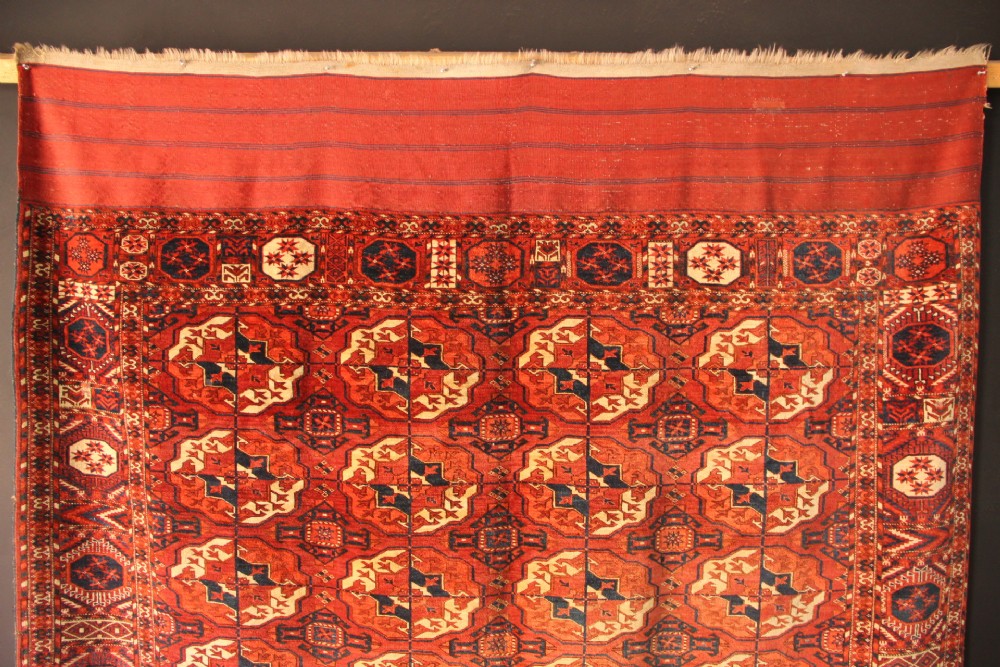 A large mid-19th century Tekke Turkoman hand-knotted wool main carpet featuring repeating geometric gol motifs on a deep red field with woven borders. View VII