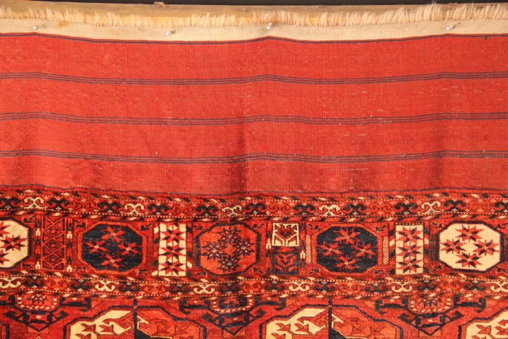 A large mid-19th century Tekke Turkoman hand-knotted wool main carpet featuring repeating geometric gol motifs on a deep red field with woven borders. View VIII