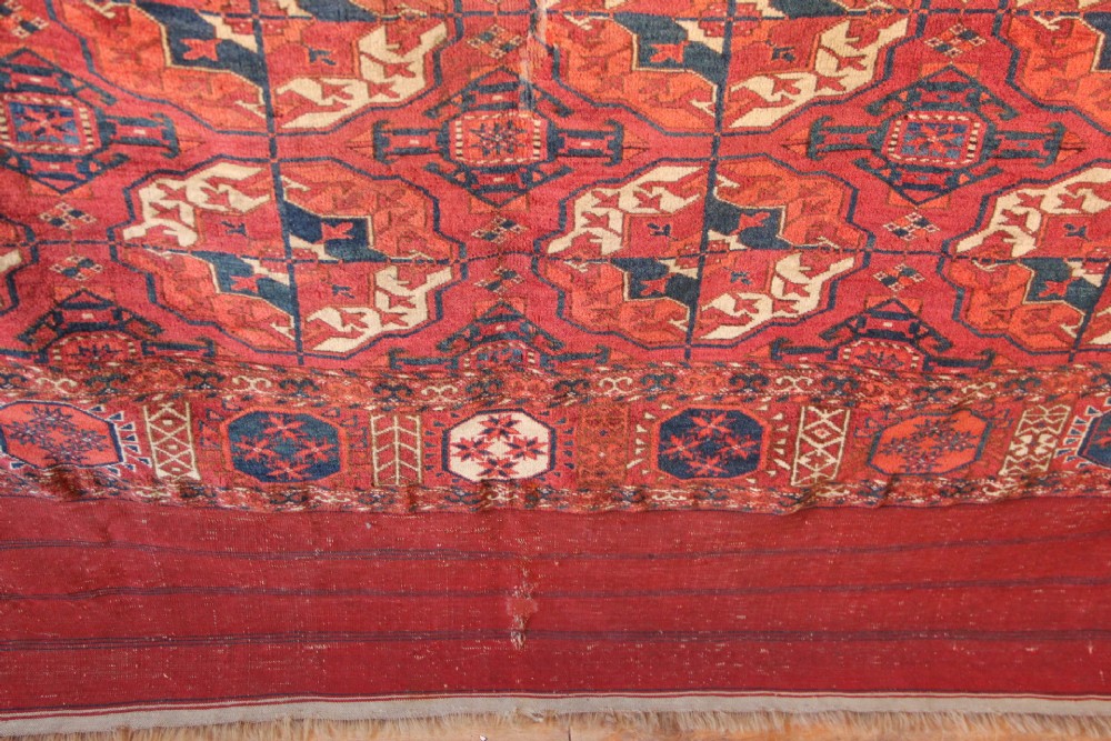 A large mid-19th century Tekke Turkoman hand-knotted wool main carpet featuring repeating geometric gol motifs on a deep red field with woven borders. View X