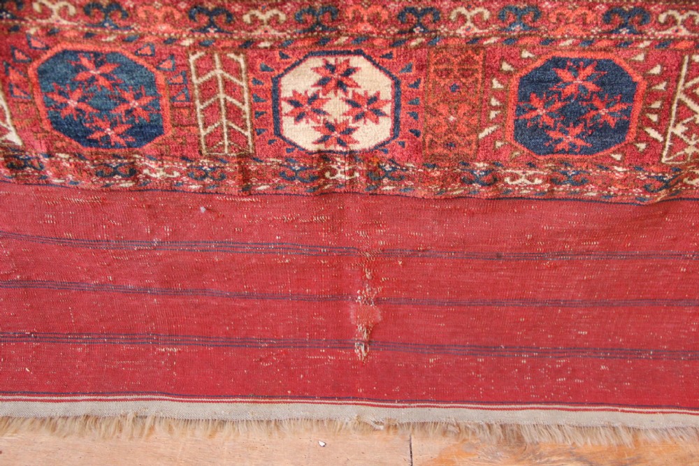 A large mid-19th century Tekke Turkoman hand-knotted wool main carpet featuring repeating geometric gol motifs on a deep red field with woven borders. View XI