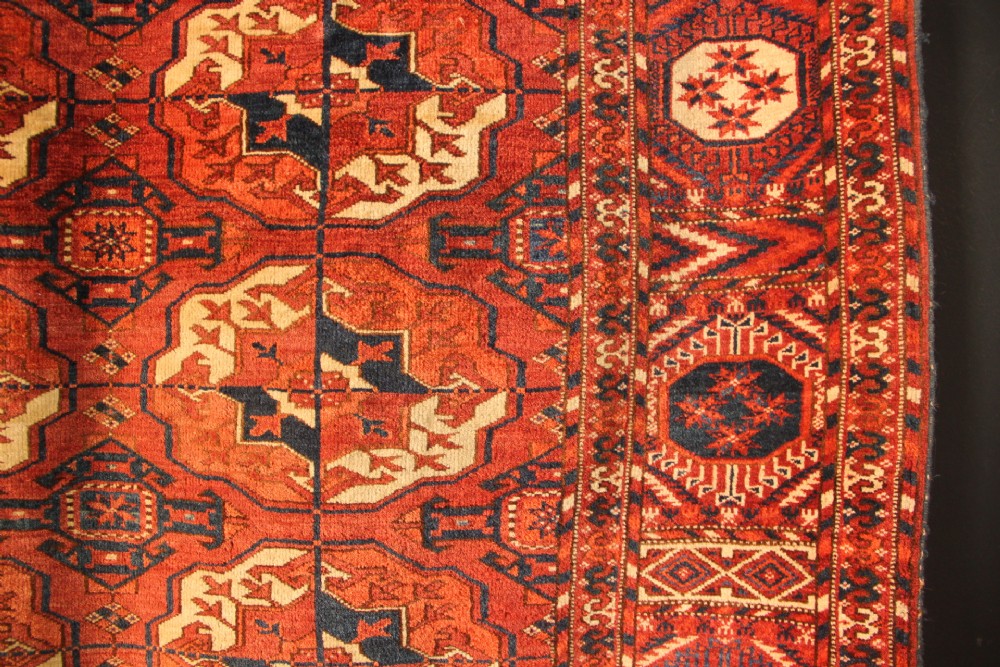 A large mid-19th century Tekke Turkoman hand-knotted wool main carpet featuring repeating geometric gol motifs on a deep red field with woven borders. View XIII