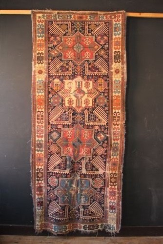A long hand-knotted antique Caucasian Akstafa wool rug featuring geometric star medallions, stylized bird motifs, and a patterned border on a navy ground.