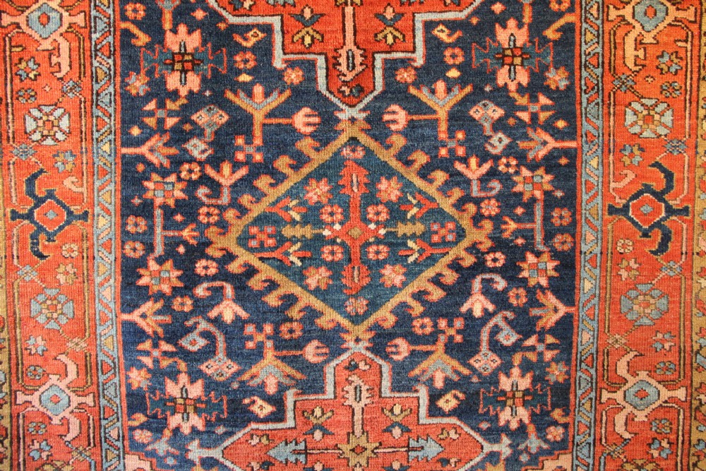 An antique hand-knotted Heriz wool rug featuring a geometric central medallion surrounded by intricate tribal patterns in terracotta red, navy blue, and cream tones. View II