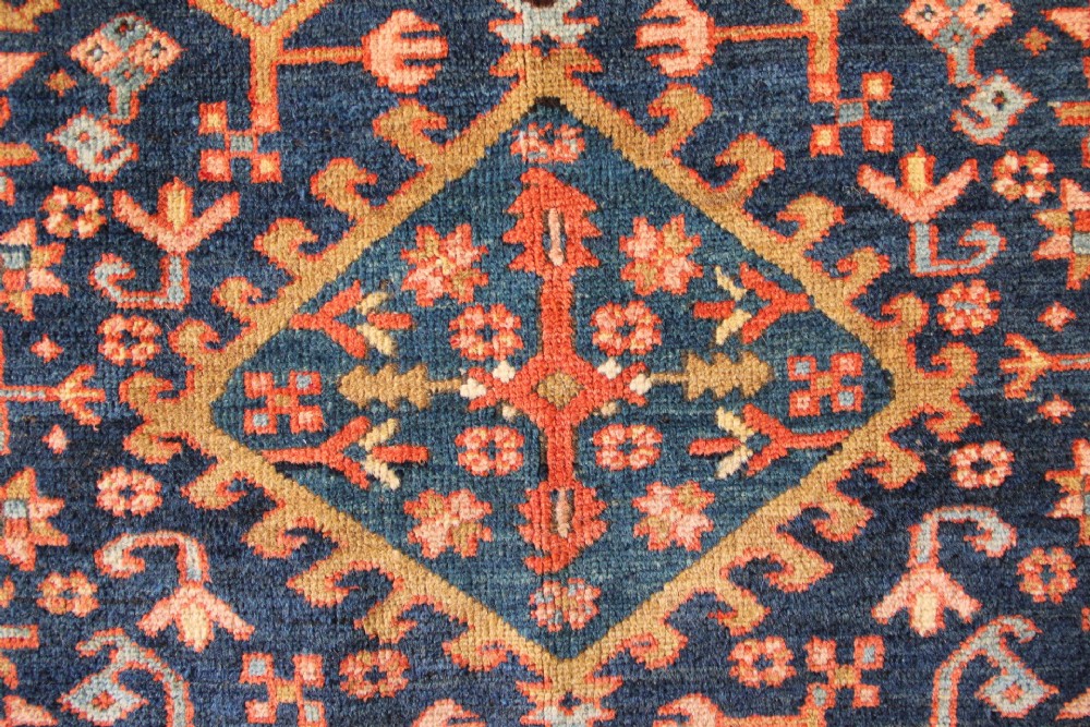 An antique hand-knotted Heriz wool rug featuring a geometric central medallion surrounded by intricate tribal patterns in terracotta red, navy blue, and cream tones. View III