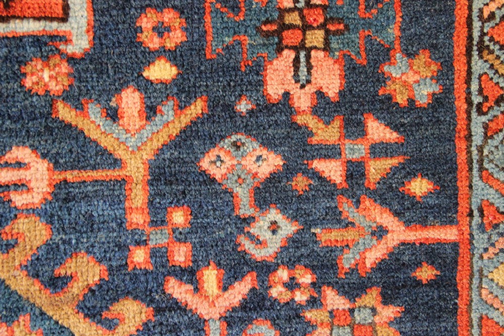 An antique hand-knotted Heriz wool rug featuring a geometric central medallion surrounded by intricate tribal patterns in terracotta red, navy blue, and cream tones. View VIII