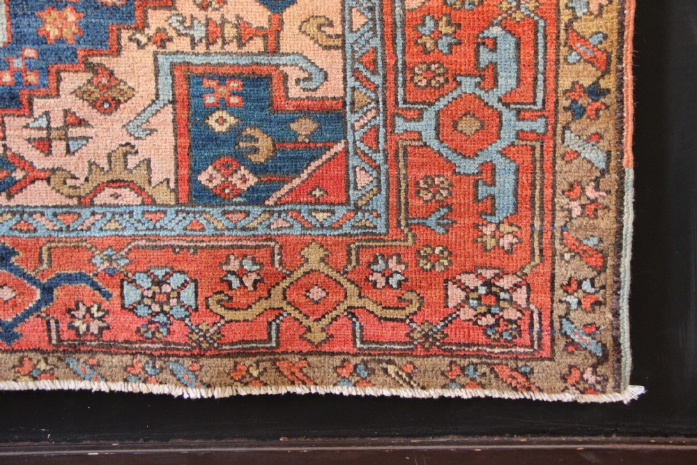 An antique hand-knotted Heriz wool rug featuring a geometric central medallion surrounded by intricate tribal patterns in terracotta red, navy blue, and cream tones. View IX