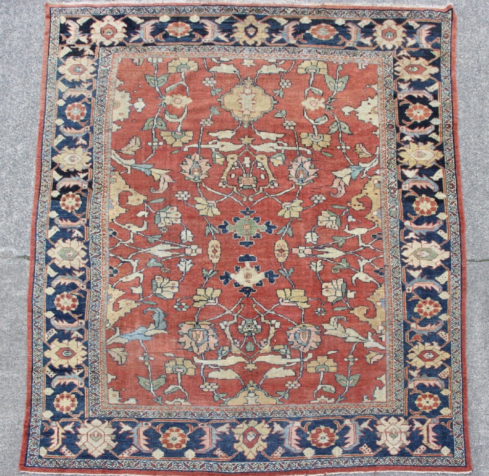 A large hand-knotted wool carpet featuring a terracotta central field with scrolling beige floral motifs framed by a wide navy blue patterned border.