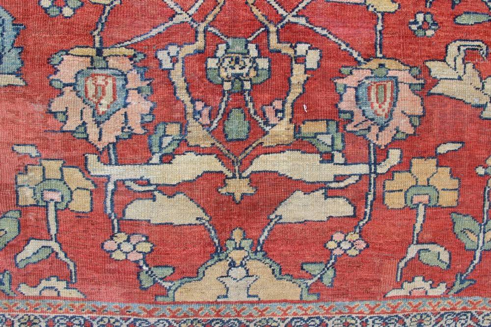A large hand-knotted wool carpet featuring a terracotta central field with scrolling beige floral motifs framed by a wide navy blue patterned border. View III