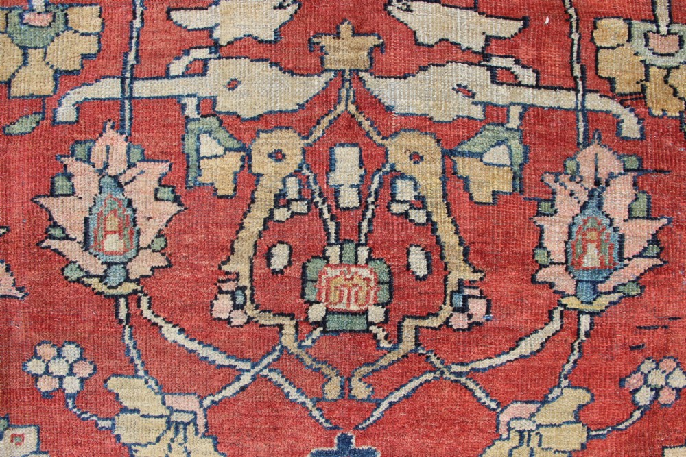 A large hand-knotted wool carpet featuring a terracotta central field with scrolling beige floral motifs framed by a wide navy blue patterned border. View VI