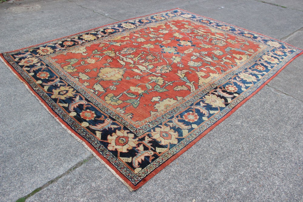 A large hand-knotted wool carpet featuring a terracotta central field with scrolling beige floral motifs framed by a wide navy blue patterned border. View XI