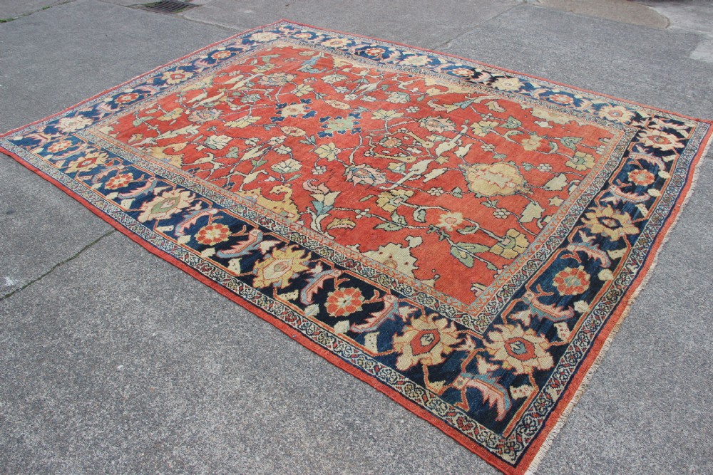 A large hand-knotted wool carpet featuring a terracotta central field with scrolling beige floral motifs framed by a wide navy blue patterned border. View XIII
