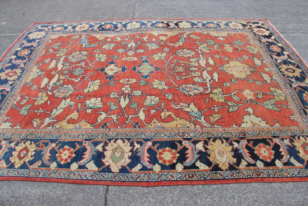 A large hand-knotted wool carpet featuring a terracotta central field with scrolling beige floral motifs framed by a wide navy blue patterned border. View XIV