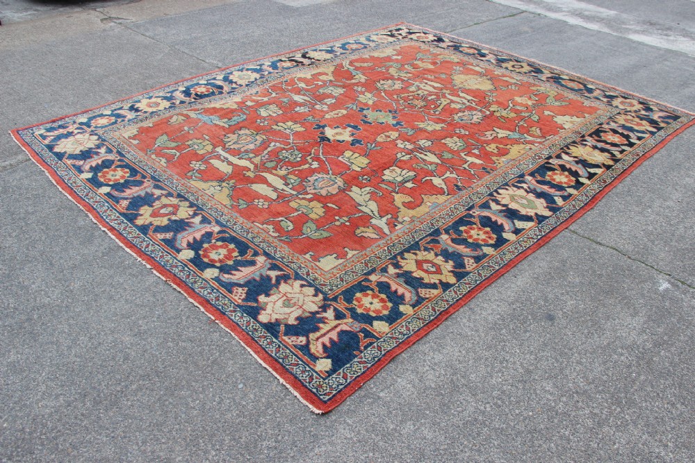 A large hand-knotted wool carpet featuring a terracotta central field with scrolling beige floral motifs framed by a wide navy blue patterned border. View XV