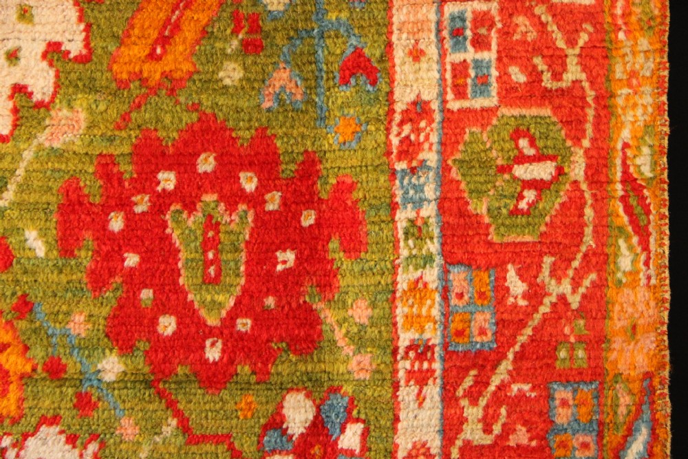 An antique hand-knotted Oushak wool rug featuring an olive green field with soft red, pink, and cream floral medallions surrounded by a terracotta patterned border. View IV