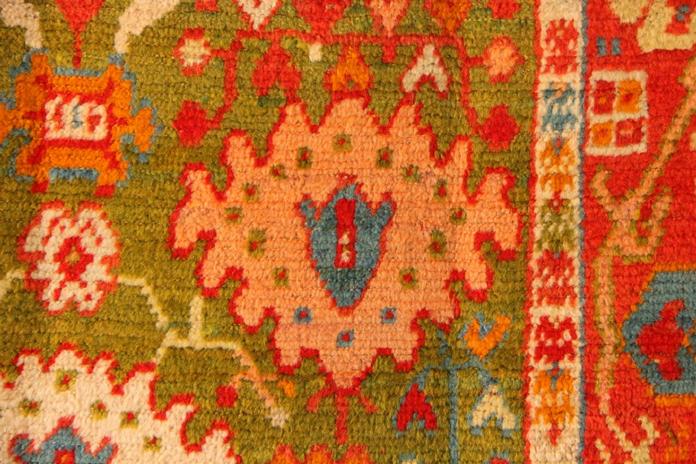 An antique hand-knotted Oushak wool rug featuring an olive green field with soft red, pink, and cream floral medallions surrounded by a terracotta patterned border. View V