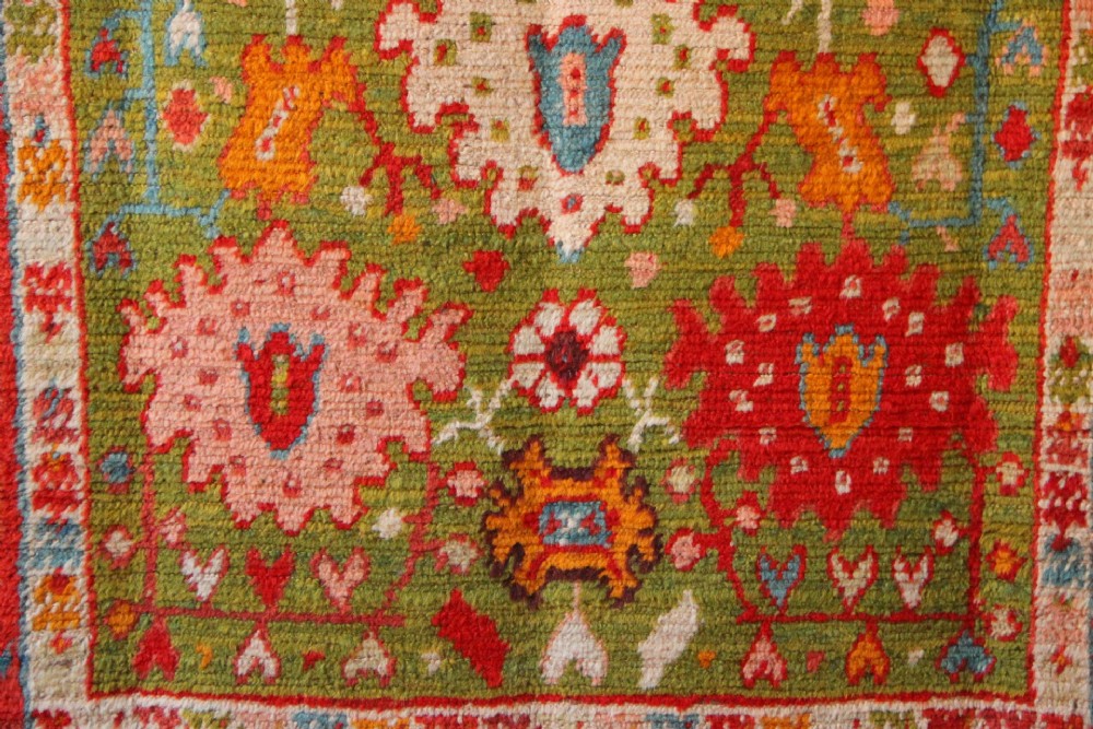 An antique hand-knotted Oushak wool rug featuring an olive green field with soft red, pink, and cream floral medallions surrounded by a terracotta patterned border. View VI